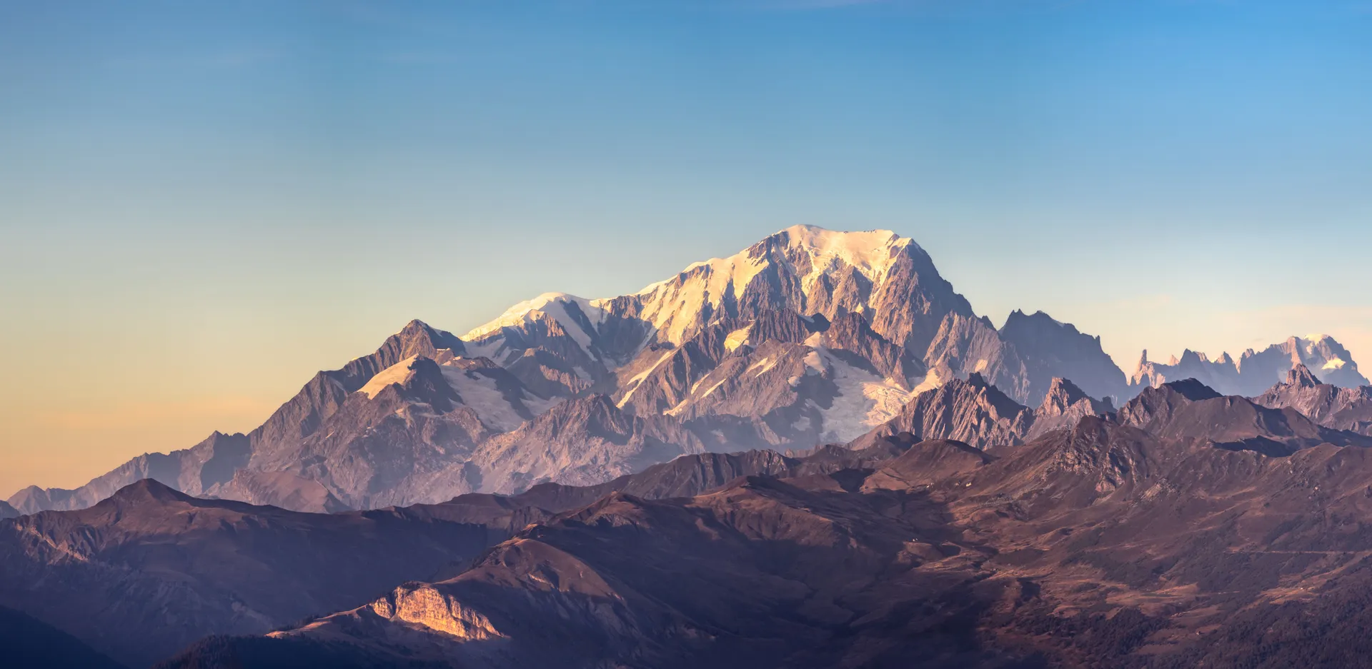 A sunlit, snow-capped mountain peak against a clear blue sky
